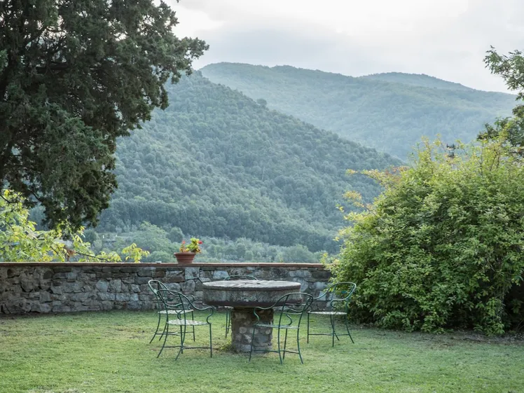Cortile con muri in pietra, mobili da patio e colline alberate che si estendono all'orizzonte