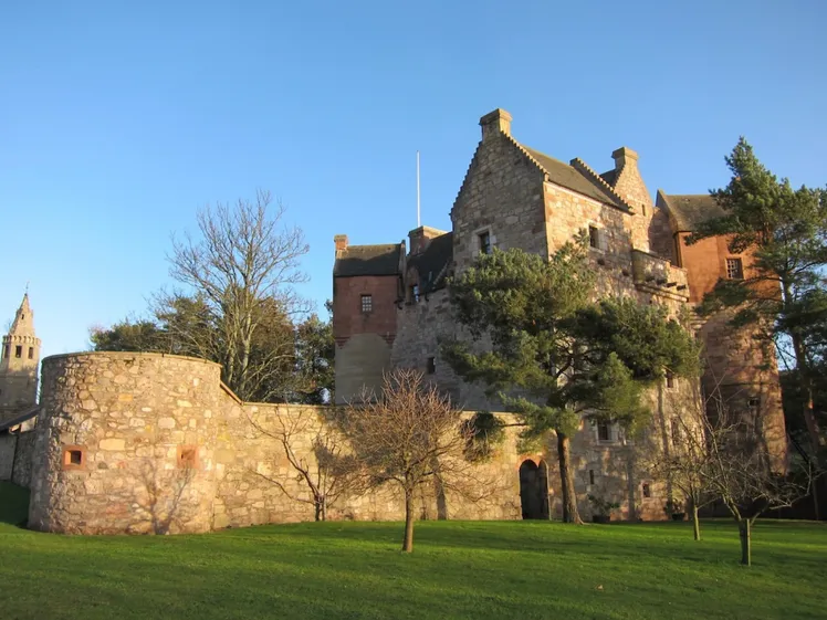 Castello in pietra con torrette e cortile circondato da alberi e giardini