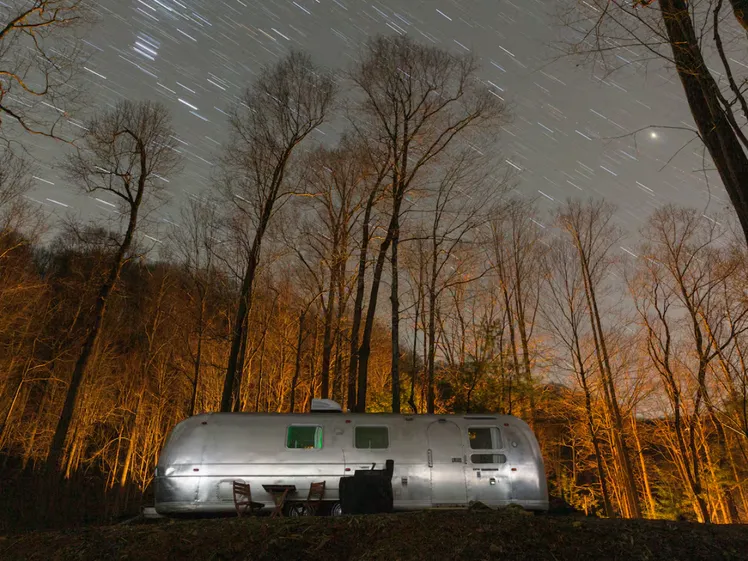 Roulotta Airstream parcheggiata tra gli alberi in montagna