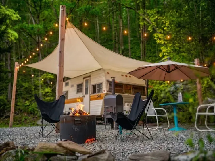 Esterno del camper vintage con tavoli e sedie parcheggiato tra gli alberi